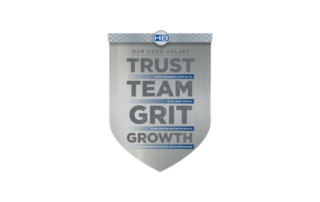 A silver badge with the HB Global core values of Trust, Team, Grit, and Growth on it.