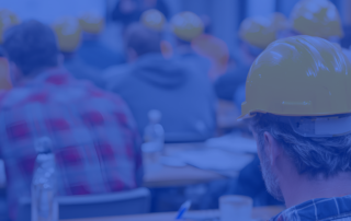A photo of construction workers with hard hats on sitting in a classroom-type setting.