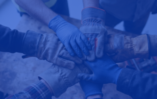 A photo of a bunch of hands wearing different types of construction gloves, coming together in a team huddle.